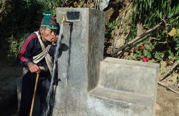 photo d'un homme en train de boire de l'eau à une fontaine dans un village népalais 