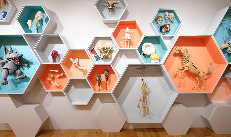 intérieur de l'exposition, des étagères en forme de rayon d'abeille avec des marionnettes à l'intérieur