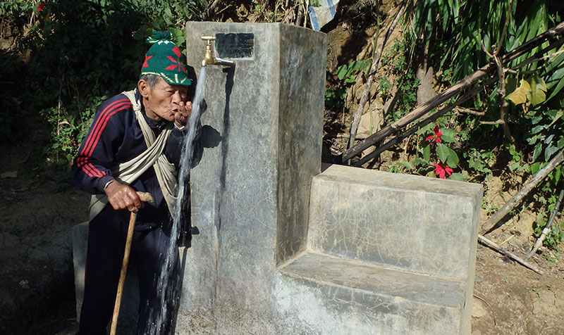 photo d'un homme en train de boire de l'eau à une fontaine dans un village népalais